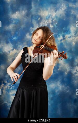 Junge Frau spielt Geige vor abstrakt blauem Hintergrund. Stockfoto