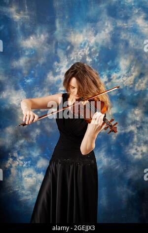 Junge Frau spielt Geige vor abstrakt blauem Hintergrund. Stockfoto