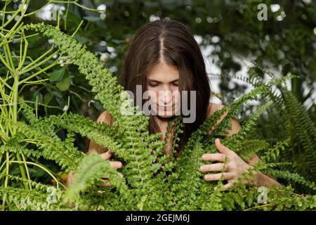 Portrait hübsches junges Mädchen umarmt Farn im verschwommenen Hintergrund des Laubwaldes Stockfoto