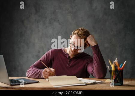 Der müde Mann, der seinen Kopf mit der Hand ruhte, während er mit Papieren im Studio am Tisch saß Stockfoto