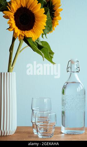 Sonnenblumen in einer Vase neben Trinkgläsern und einer Wasserkaraffe. Stockfoto