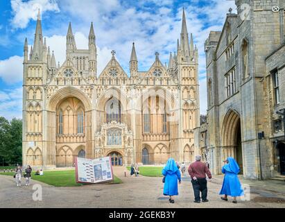 Ein englischer Priester und zwei afrikanische Nonnen gehen in Richtung der Westwand der mittelalterlichen christlichen Kathedrale in Peterborough, England, aus dem 13. Jahrhundert. Stockfoto