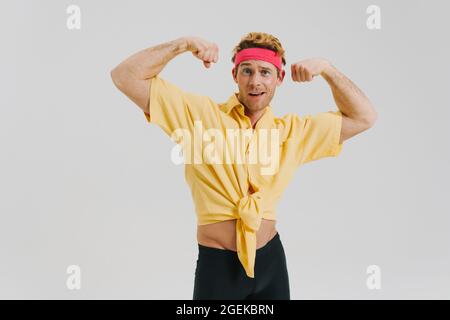 Junge weiße Homosexuell Mann trägt Stirnband biegen Bizeps stehen über grauen Wand Hintergrund Blick auf Kamera Stockfoto