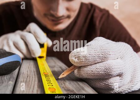 Reparatur-, Bau- und Hauskonzept - Nahaufnahme von männlichen Händen, die Holzbretter messen. Der professionelle Zimmermann misst präzise mit einem gelben Hahn Stockfoto