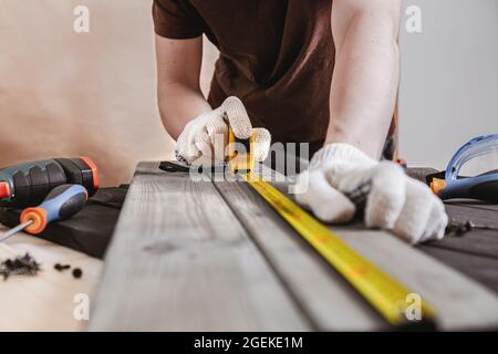 Reparatur-, Bau- und Hauskonzept - Nahaufnahme von männlichen Händen, die Holzbretter messen. Der professionelle Zimmermann misst präzise mit einem gelben Hahn Stockfoto