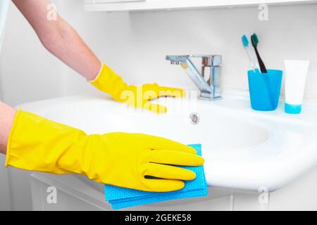 Frau, die im Badezimmer Hausarbeiten macht, den Wasserhahn oder das Waschbecken und den Wasserhahn reinigt. Konzept tägliche Hygiene des Badezimmers Stockfoto