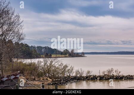 Jamestowne, VA, USA - 1. April 2013: Historische Stätte. Graues Wasser James River unter blauer Wolkenlandschaft mit braunen und grünen Laubbäumen am Ufer. Schleife Stockfoto
