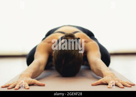 Yogi-Frau praktiziert die Kinderpose im hellen Studio. Konzentrieren Sie sich auf die Hände einer Dame in Balasana auf rosa Matte. Gesunder Lebensstil, Ausruhen, Training, Sport Stockfoto