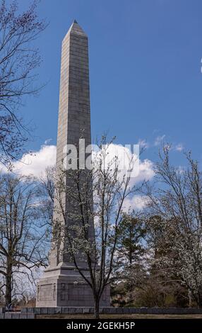 Jamestowne, VA, USA - 1. April 2013: Historische Stätte. Tencentennial Monument umgeben von blühenden Bäumen unter blauer Wolkenlandschaft. Stockfoto