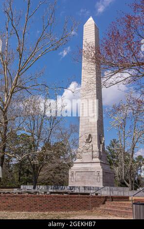 Jamestowne, VA, USA - 1. April 2013: Historische Stätte. Nahaufnahme des Tencentennial-Denkmals, umgeben von blühenden Bäumen unter blauer Wolkenlandschaft. Stockfoto