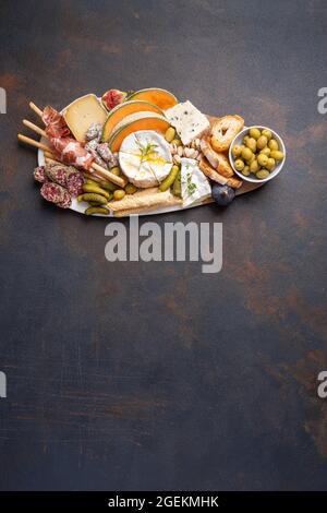 Verschiedene Käsesorten auf Holzbrettteller, Oliven, Trauben, Brot auf schwarzem Stein-Hintergrund, Draufsicht, flaches Lay, Kopierraum. Stockfoto