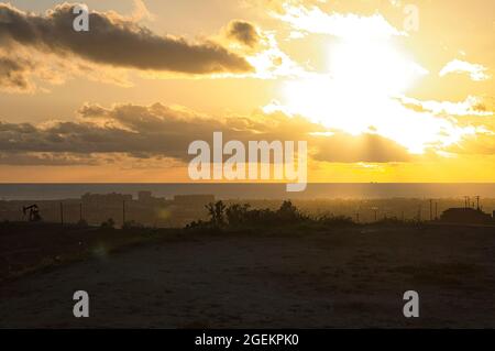 Am späten Nachmittag strömt Sonnenlicht durch Wolken bei Sonnenuntergang über dem grasbewachsenen Strand Stockfoto