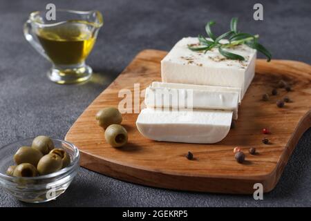 Feta-Käse befindet sich auf einem Holzbrett mit Oliven, Rosmarin und Olivenöl auf dunklem Hintergrund Stockfoto