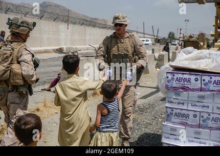 Ein Korpsmann der US-Marine mit der Special Purpose Marine Air-Ground Task Force - Crisis Response - Central Command gibt Kindern während einer Evakuierung am Hamid Karzai International Airport, Kabul, Afghanistan, am 20. August Wasser aus. US-Dienstmitglieder unterstützen das Außenministerium bei einer geordneten Abseichung von designiertem Personal in Afghanistan. (USA Marine Corps Foto von Lance CPL. Nichola Guevara) Stockfoto
