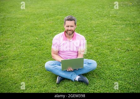 Freelance Mann post Blog online sitzen auf Gras. Schreiben online. Geschäftsmann mit Laptop zum Bloggen Stockfoto