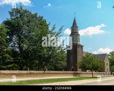 Williamsburg, VA, USA - 20. Juni 2006: Historische Stätte. Bruton Episcopal Pfarrkirche mit in seinem Park gegen blaue Wolkenlandschaft gesetzt. Besucher auf der Straße. Stockfoto