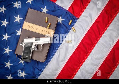 Eine Waffe und eine heilige bibel stehen auf einer amerikanischen Flagge, die Gott, Waffen und Religionsfreiheit repräsentiert. Stockfoto