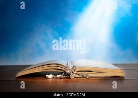 Dramatisches Bild mit einem hellen Lichtstrahl, der auf eine alte bibel mit einem Rosenkranz vor ihr scheint. Stockfoto