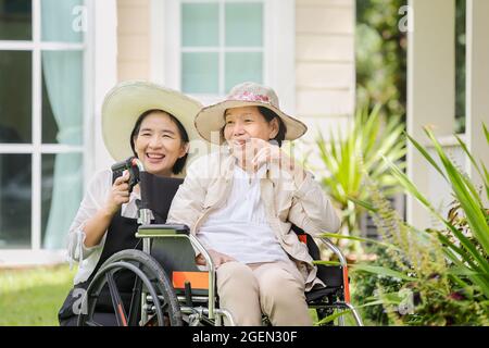 Ältere Frau entspannen sich im Rollstuhl im Hinterhof mit Tochter Stockfoto