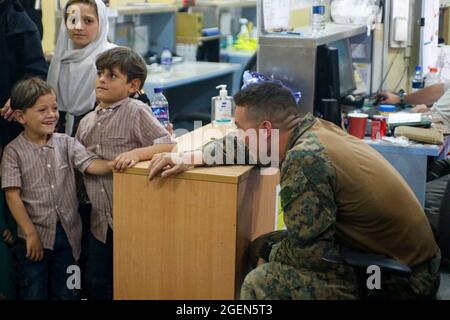 Eine US-Marine, die der 24. Marine Expeditionary Unit zugeordnet ist, interagiert mit Kindern während einer Evakuierung am Hamid Karzai International Airport, Afghanistan, 18. August 2021. US-Dienstmitglieder unterstützen das US-Außenministerium bei einer geordneten Abseichung von designiertem Personal in Afghanistan. Obligatorische Gutschrift: Nichola Guevara/US Marine Corps über CNP Stockfoto