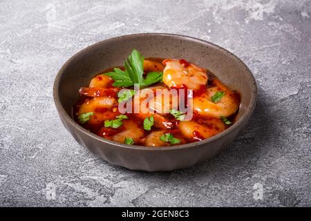 Schüssel mit würzigen Garnelen in süßer Chili-asiatischer roter Sauce auf grauem Betonboden Stockfoto