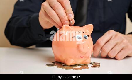 Man Hand hält Bronzemünzen und wirft in Sparschwein Slot Stockfoto