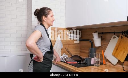 Verstörte Frau kommt in die Küche und sieht schmutziges Geschirr im Waschbecken Stockfoto
