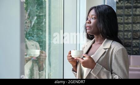 Afroamerikanische Frau trinkt Kaffee in der Nähe des Fensters im Büro Stockfoto