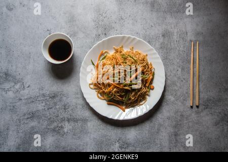 Schezwan-Nudeln, die mit gehacktem Gemüse, Fleisch und udon-Nudeln auf einem weißen Teller zubereitet werden. Draufsicht. Stockfoto