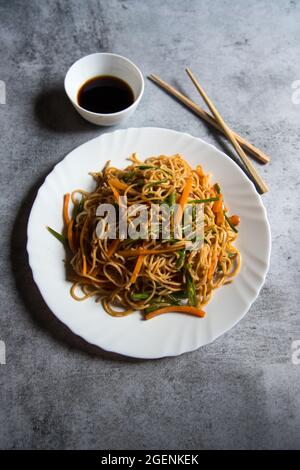 Schezwan-Nudeln, die mit gehacktem Gemüse, Fleisch und udon-Nudeln auf einem weißen Teller zubereitet werden. Stockfoto