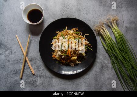 Schezwan-Nudeln, die mit gehacktem Gemüse, Fleisch und udon-Nudeln auf einem weißen Teller zubereitet werden. Blick von oben. Stockfoto