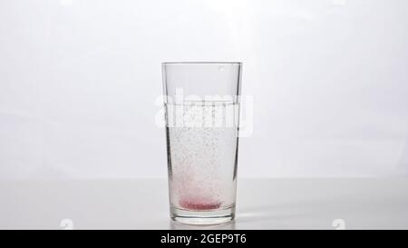 Brausetablette fällt auf weißem Grund in ein Glas Wasser Stockfoto