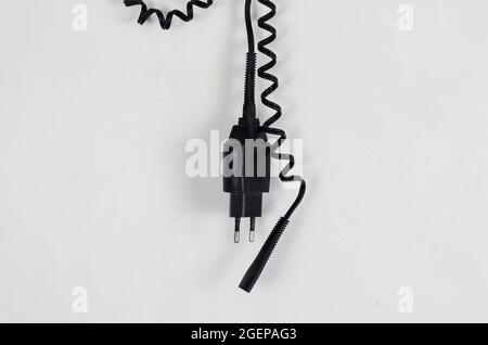An der weißen Wand hängt ein schwarzes Stromkabel mit Spiraldraht. Ein Ladegerät für einen elektrischen Rasierer. Seitenansicht. Stockfoto