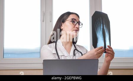 Arzt mit Brille prüft Röntgenbild der Füße im Büro Stockfoto