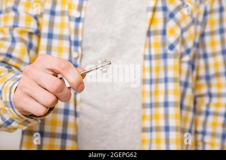 Der junge Mann macht eine Geste, die Tür zu öffnen und hält den Schlüssel im Zimmer Stockfoto