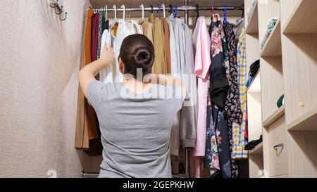 Die junge Frau wählt Kleidung in einem modernen begehbaren Kleiderschrank Stockfoto