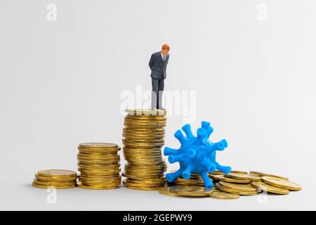 Business und Pandemie. Das Coronavirus hat einen Münzstapel zerstört, auf dem ein Geschäftsmann in einem Anzug steht. Stockfoto