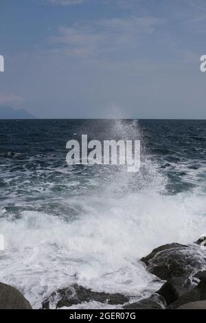 Eine Welle, die gegen einen Felsen stürzt und in Chalkidiki Griechenland einen großen Spritzer in der Luft erzeugt Stockfoto