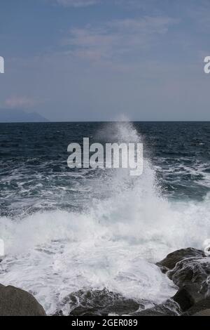 Eine Welle, die gegen einen Felsen stürzt und in Chalkidiki Griechenland einen großen Spritzer in der Luft erzeugt Stockfoto