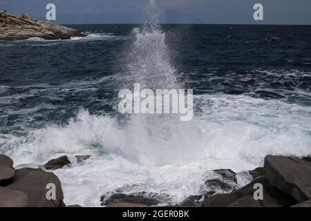 Eine Welle, die gegen einen Felsen stürzt und in Chalkidiki Griechenland einen großen Spritzer in der Luft erzeugt Stockfoto