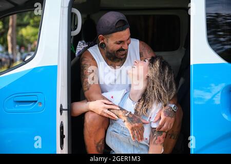 Das junge tätowierte Paar lacht und schaut sich an der Seite des Wagens an. Stockfoto