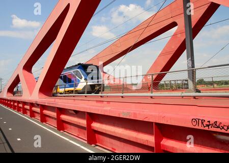 Der Regionalpendler SNG fährt über die rote Hanzeboog-Stahlbrücke über den Fluss IJssel in der Nähe von Zwolle in den Niederlanden Stockfoto