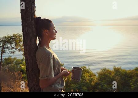 Frau, die sich mit einer Tasse Tee gegen den Baum lehnt Stockfoto
