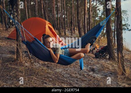 Camper chillt in ihrer blauen Hängematte in der Nähe des Zeltes Stockfoto