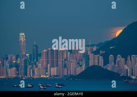 Der Vollmond steigt hinter dem Victoria Peak und der Skyline von Kennedy Town und Central, Hong Kong Island, auf Stockfoto