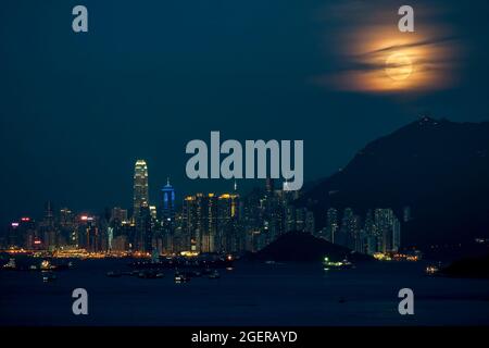 Der Vollmond steigt hinter dem Victoria Peak und der Skyline von Kennedy Town und Central, Hong Kong Island, auf Stockfoto