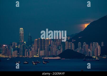 Der Vollmond steigt hinter dem Victoria Peak und der Skyline von Kennedy Town und Central, Hong Kong Island, auf Stockfoto