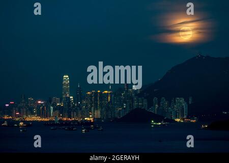 Der Vollmond steigt hinter dem Victoria Peak und der Skyline von Kennedy Town und Central, Hong Kong Island, auf Stockfoto