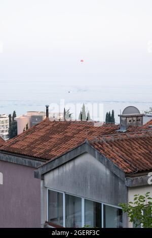 Blick auf einen weit entfernten Parasailer, der über das Meer und die Dächer von Becici, Montenegro, vor einem bunten Himmel fliegt Stockfoto