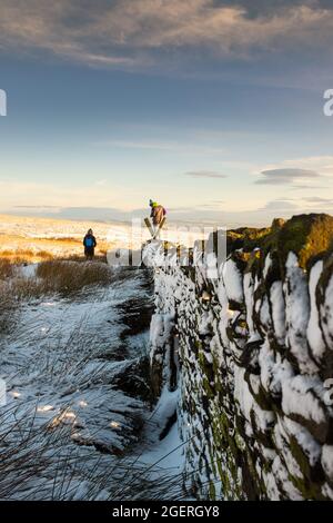 Wanderer klettern an einem verschneiten Wintertag über einen Stiel an einer trockenen Steinmauer Stockfoto